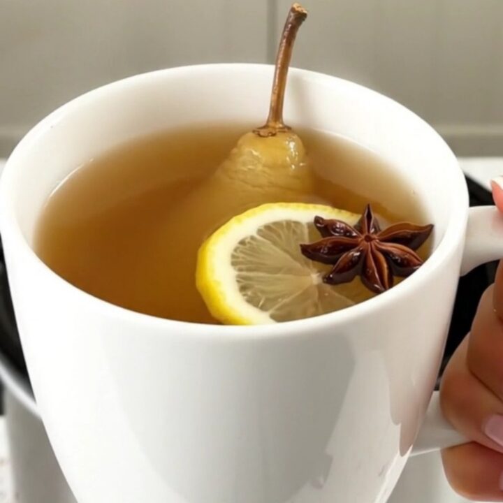 A steaming mug of spiced pear juice with a cinnamon stick and star anise, set against a blurred kitchen background.