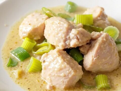 A steaming, creamy chicken and leek dish served on a clean, round white plate.