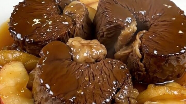 Slow cooked cider braised beef cheeks served on a white plate with tender apple wedges.