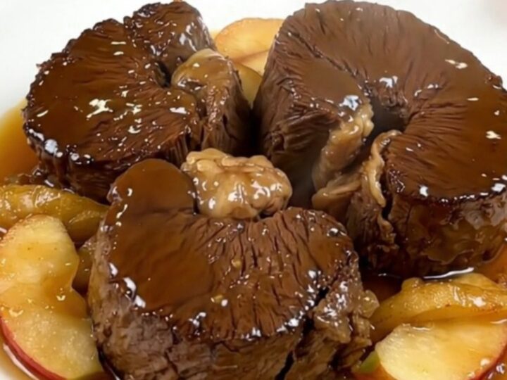Slow cooked cider braised beef cheeks served on a white plate with tender apple wedges.