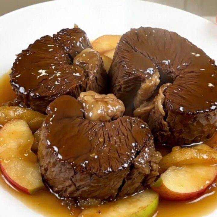 Slow cooked cider braised beef cheeks served on a white plate with tender apple wedges.