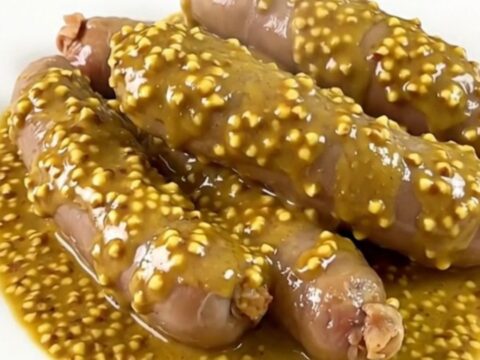 Quatre andouillettes nappées d'une sauce moutardée brillante servies dans une assiette blanche.
