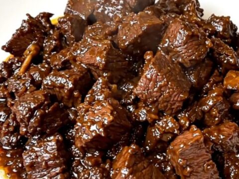 A close-up of tender beef rendang in a black slow cooker on a white quartz countertop.