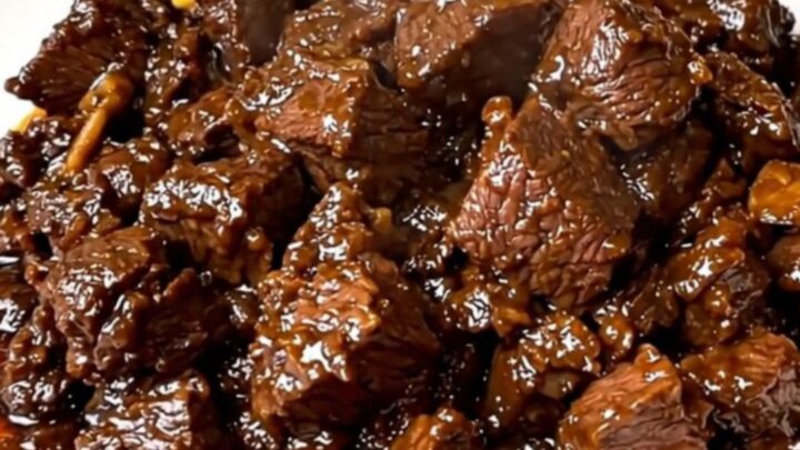 A close-up of tender beef rendang in a black slow cooker on a white quartz countertop.