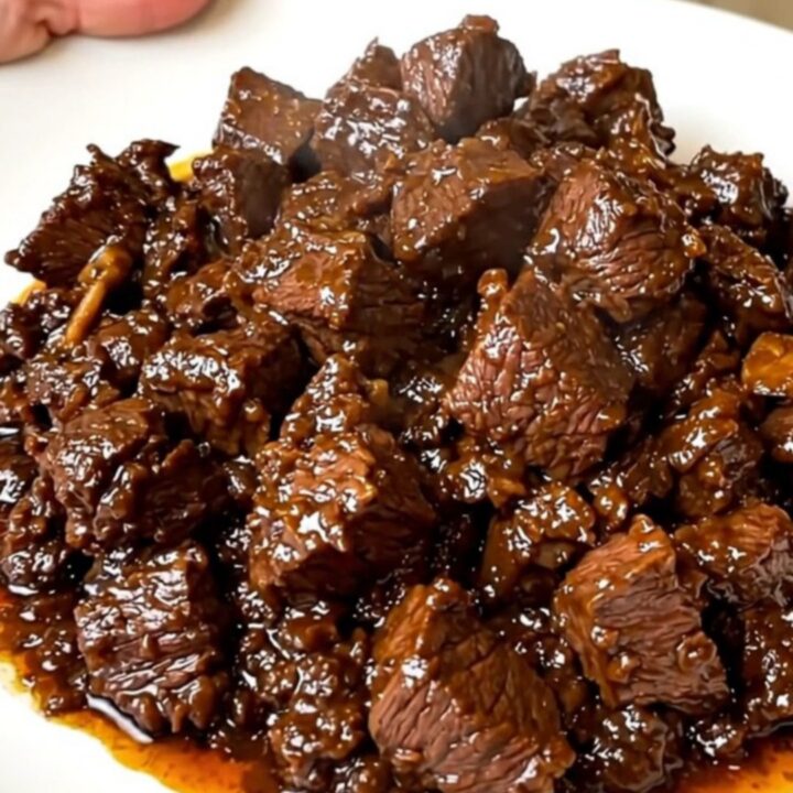 A close-up of tender beef rendang in a black slow cooker on a white quartz countertop.