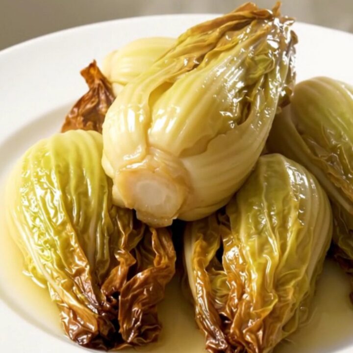 A plate of golden, tender braised endives with a light buttery glaze.