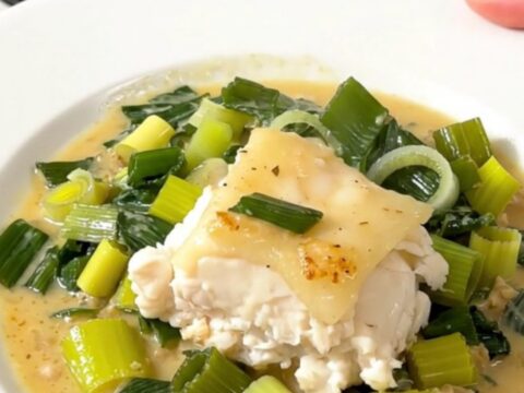 A close-up of a perfectly cooked, flaky cod fillet topped with a creamy leek sauce on a white plate.