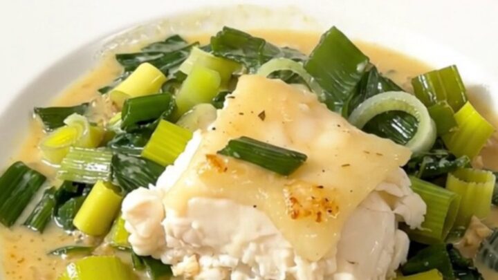 A close-up of a perfectly cooked, flaky cod fillet topped with a creamy leek sauce on a white plate.