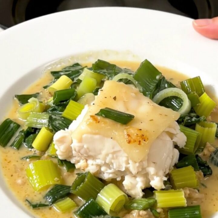 A close-up of a perfectly cooked, flaky cod fillet topped with a creamy leek sauce on a white plate.