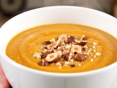 Bol de soupe de potimarron orange vif, garni de noisettes concassées sur un fond de cuisine clair.