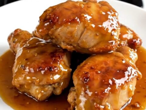 Vue de dessus d'une mijoteuse avec des hauts de cuisse de poulet enrobés d'une sauce brillante au miel et à la moutarde.