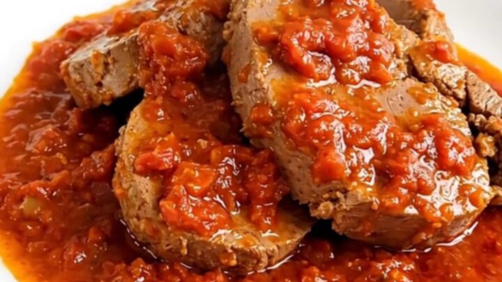 A steaming, glossy portion of slow-cooked veal in a rich Provencal tomato sauce served on a round white plate.