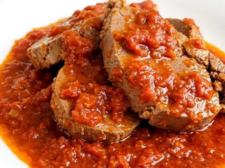 A steaming, glossy portion of slow-cooked veal in a rich Provencal tomato sauce served on a round white plate.