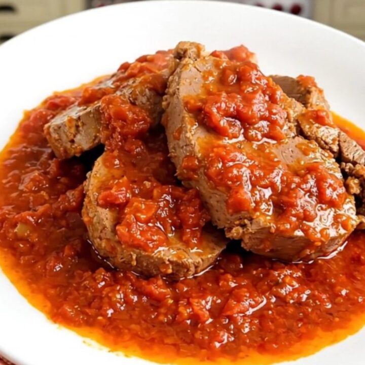 A steaming, glossy portion of slow-cooked veal in a rich Provencal tomato sauce served on a round white plate.