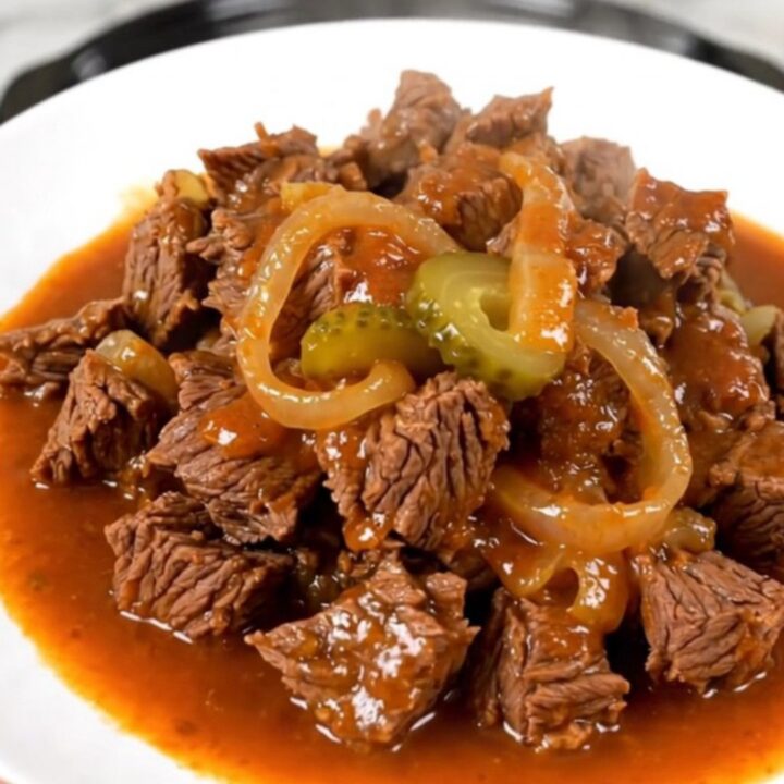 A close-up of a steaming, glossy beef miroton served on a white plate with onion and pickle slices visible.