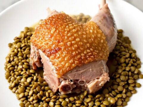 Cuisses de canard confites avec des lentilles vertes et des carottes dans une mijoteuse sur un plan de travail.