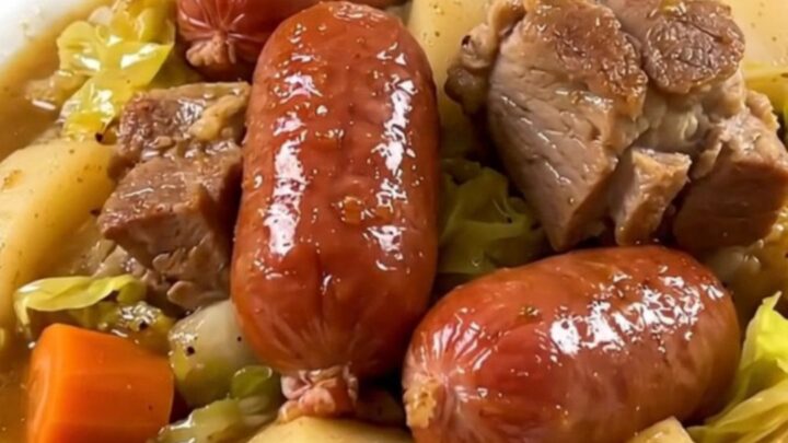 A rustic Breton pork and cabbage stew in a black slow cooker on a white quartz countertop.