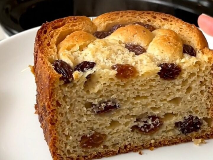 A slow cooker filled with freshly made bread pudding topped with raisins.