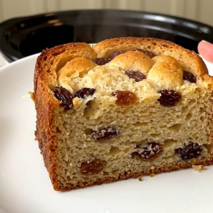 A slow cooker filled with freshly made bread pudding topped with raisins.