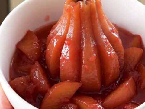 A white bowl filled with glossy, rosy quince and apple compote, steaming gently in a bright kitchen.