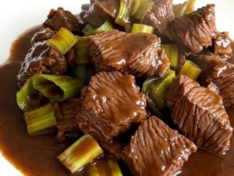 A close-up of a tender slow-cooked beef and leek dish served on a white plate.