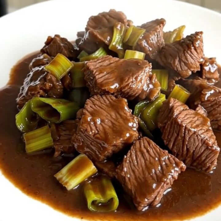 A close-up of a tender slow-cooked beef and leek dish served on a white plate.