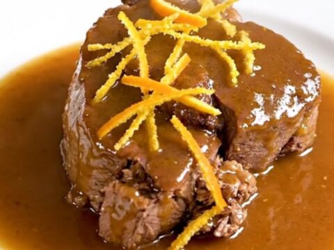 A close-up of tender citrus veal osso buco on a white plate with a glossy sauce.