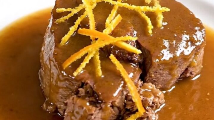 A close-up of tender citrus veal osso buco on a white plate with a glossy sauce.