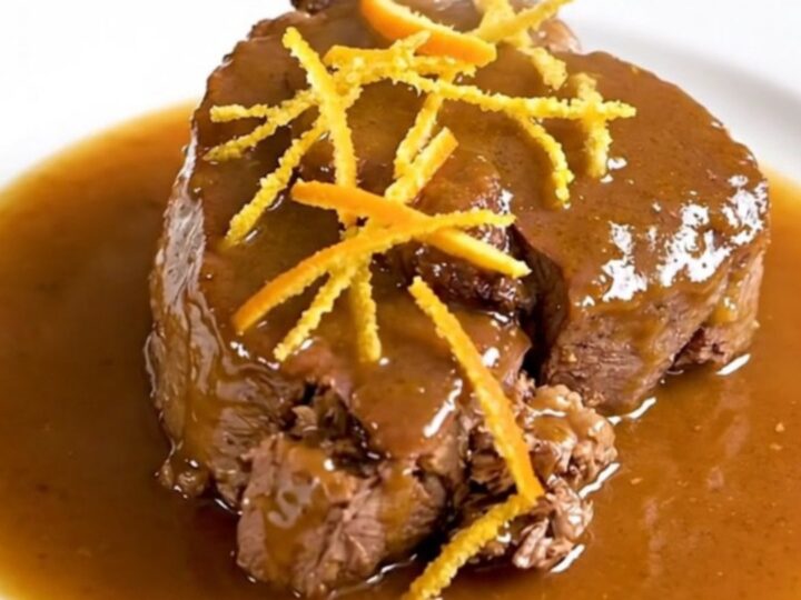 A close-up of tender citrus veal osso buco on a white plate with a glossy sauce.