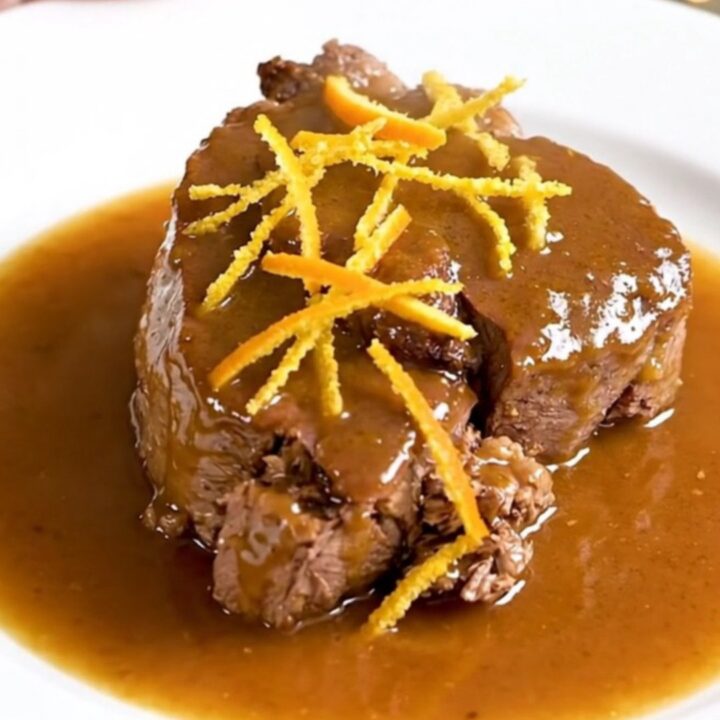 A close-up of tender citrus veal osso buco on a white plate with a glossy sauce.