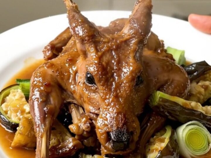 A white plate featuring tender braised rabbit pieces surrounded by glazed carrots, leeks, and onions in a light cider sauce.