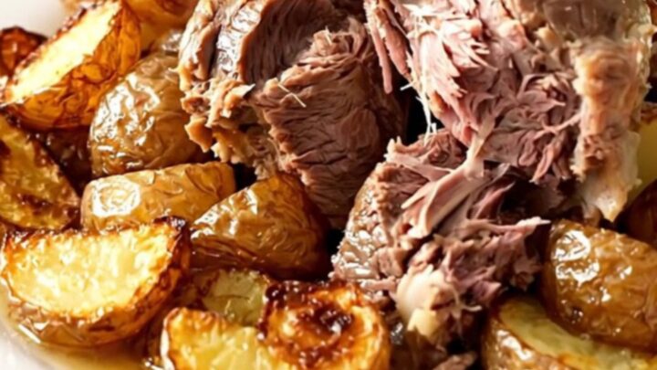 A rustic slow cooker lamb boulangère with tender potatoes and onions in a black oval pot.