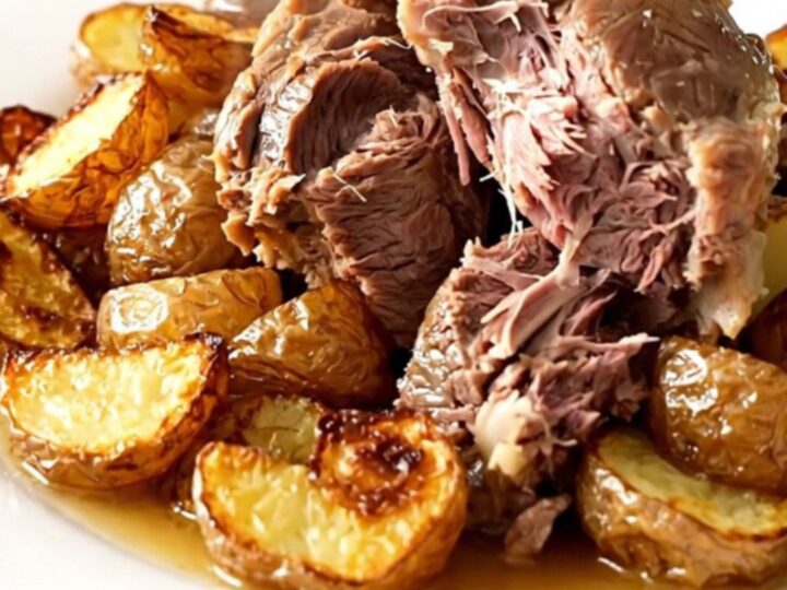 A rustic slow cooker lamb boulangère with tender potatoes and onions in a black oval pot.