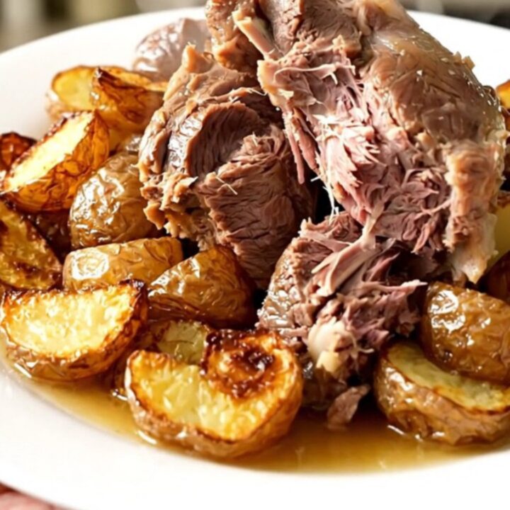 A rustic slow cooker lamb boulangère with tender potatoes and onions in a black oval pot.