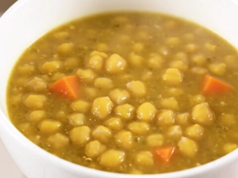 A steaming white bowl filled with thick, creamy split pea and vegetable stew on a kitchen counter.