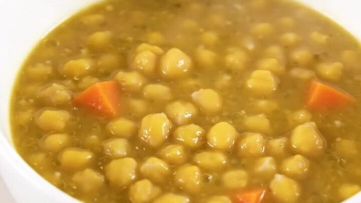 A steaming white bowl filled with thick, creamy split pea and vegetable stew on a kitchen counter.