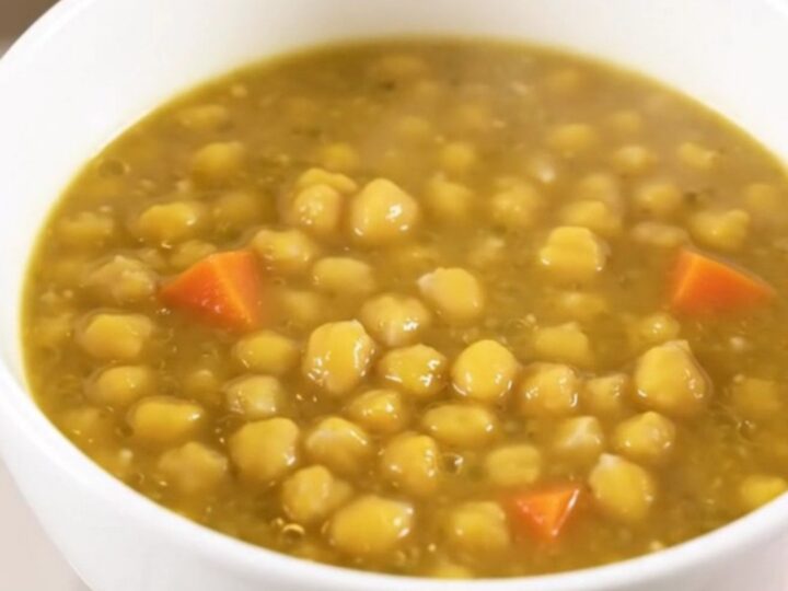 A steaming white bowl filled with thick, creamy split pea and vegetable stew on a kitchen counter.