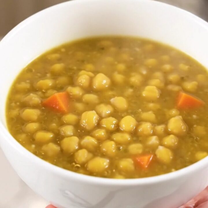 A steaming white bowl filled with thick, creamy split pea and vegetable stew on a kitchen counter.