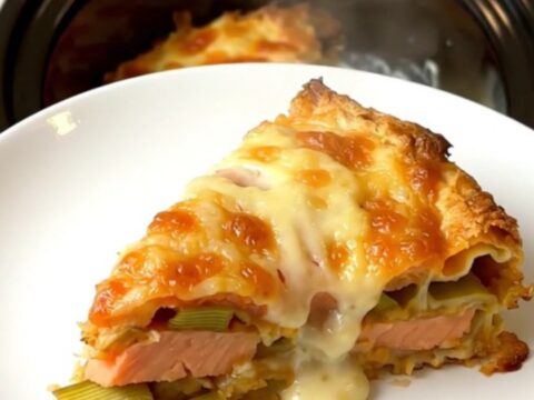 A top-down view of a slow cooker filled with layers of salmon, leeks, and creamy béchamel lasagna.