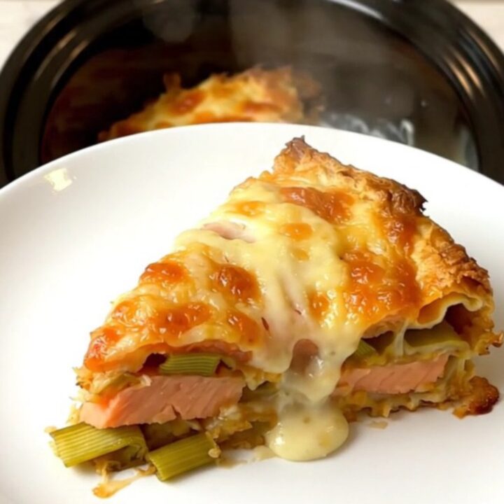 A top-down view of a slow cooker filled with layers of salmon, leeks, and creamy béchamel lasagna.
