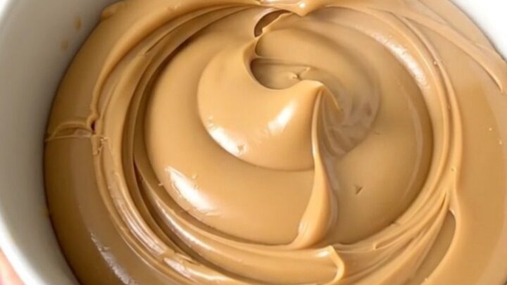 A glossy, creamy white chocolate hazelnut spread in a white bowl on a kitchen counter.