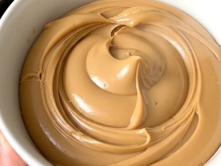 A glossy, creamy white chocolate hazelnut spread in a white bowl on a kitchen counter.