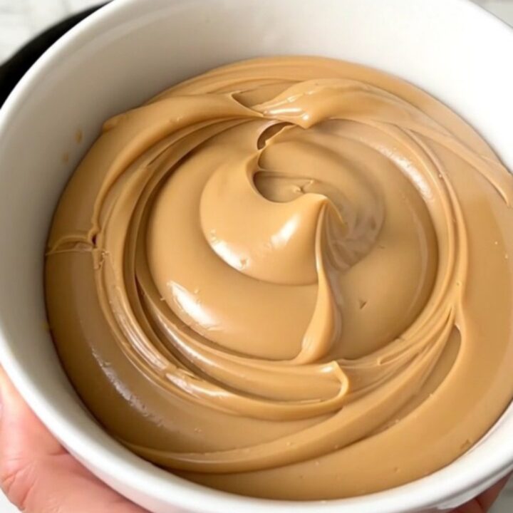 A glossy, creamy white chocolate hazelnut spread in a white bowl on a kitchen counter.