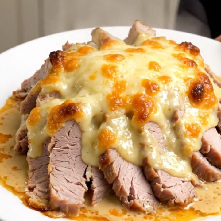 A succulent slow cooker pork roast Orloff sliced and served on a white plate with creamy sauce.