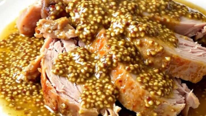 A close-up of tender turkey cubes in a creamy mustard sauce inside a black slow cooker.