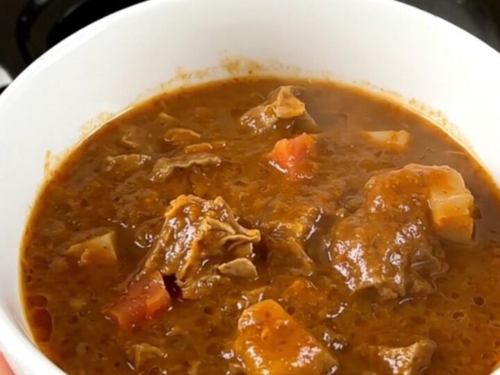 Une garbure landaise servie dans un bol en céramique blanc, avec le bouillon brillant et des morceaux de viande tendres.