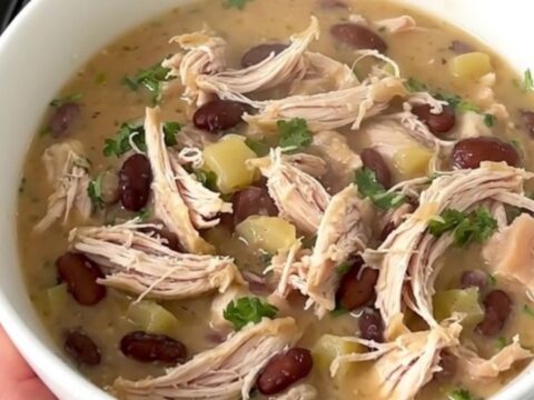 A top-down view into a black slow cooker showing raw chicken, white beans, and broth being prepared for cooking.