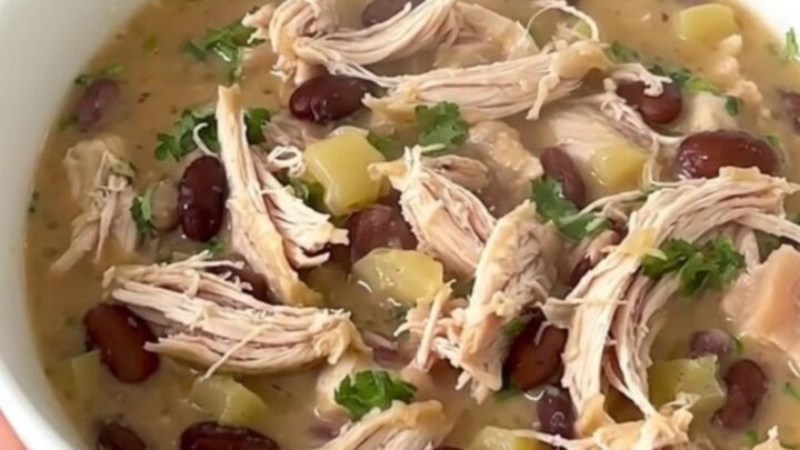 A top-down view into a black slow cooker showing raw chicken, white beans, and broth being prepared for cooking.