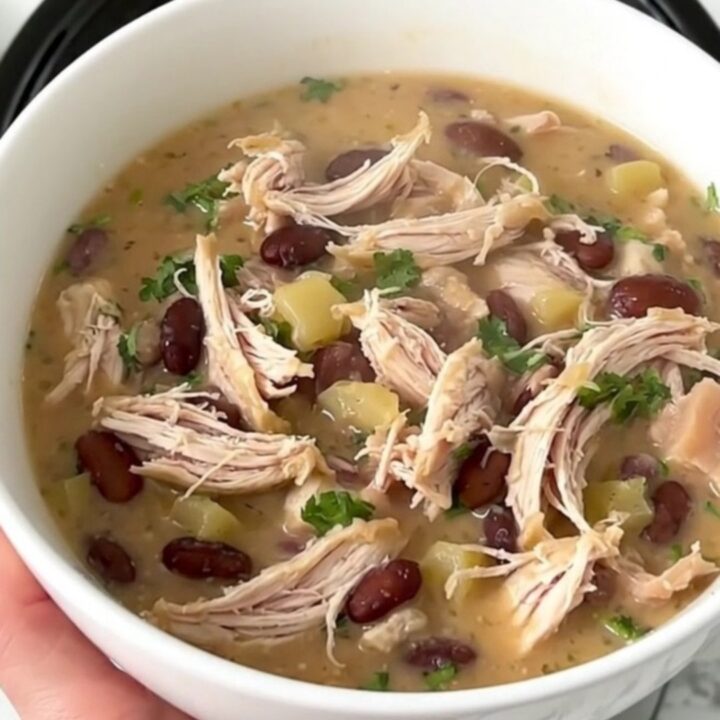 A top-down view into a black slow cooker showing raw chicken, white beans, and broth being prepared for cooking.