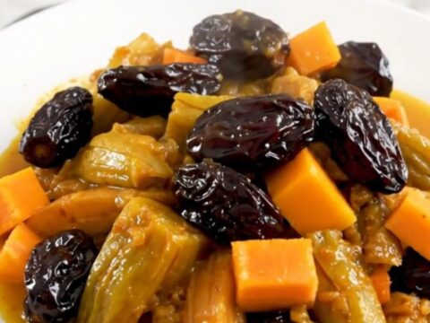 A steaming, glossy vegetarian tagine with squash, carrots, and prunes served on a white plate.